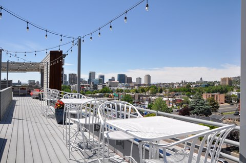 A rooftop patio with white chairs and tables overlooking a city skyline.