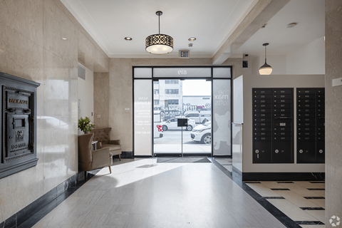 A hallway with a black and white checkered floor, a black door, and a white wall with a framed picture on it.