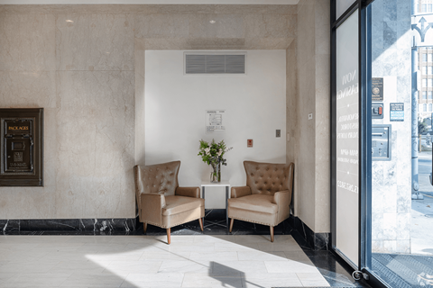 Two tan chairs are placed in front of a wall with a framed picture.