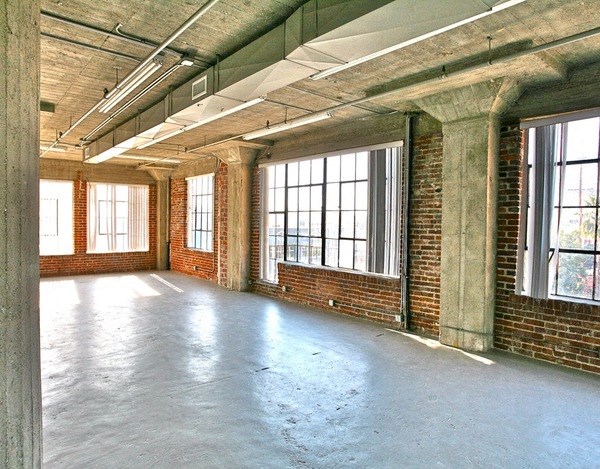 an empty room with large windows and a concrete floor at Binford Lofts Apartments, California, 90013