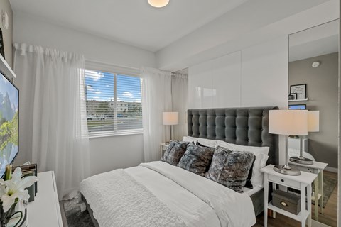 A bedroom with a large bed, a nightstand with a lamp, and a TV on the wall.