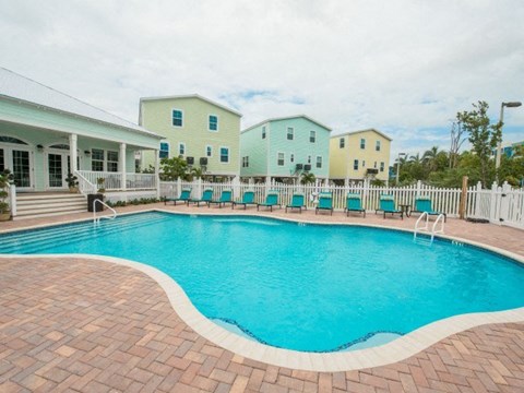 A pool surrounded by a brick border with chairs around it.