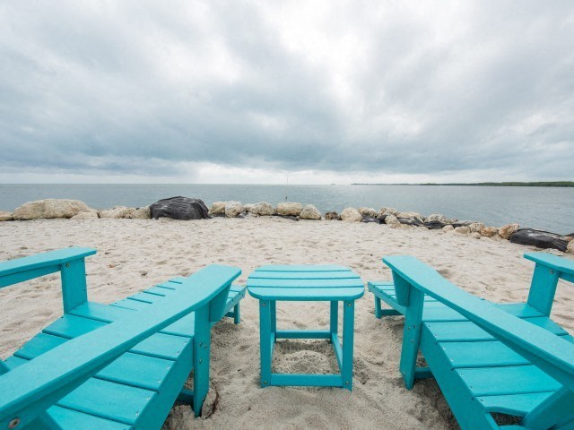 A beach scene with blue chairs and a table.