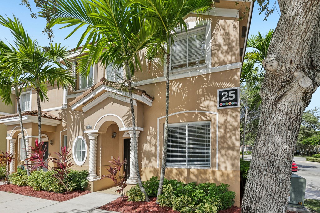 A beige house with a tree in front.