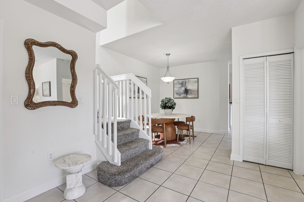 A white hallway with a staircase and a mirror on the wall.