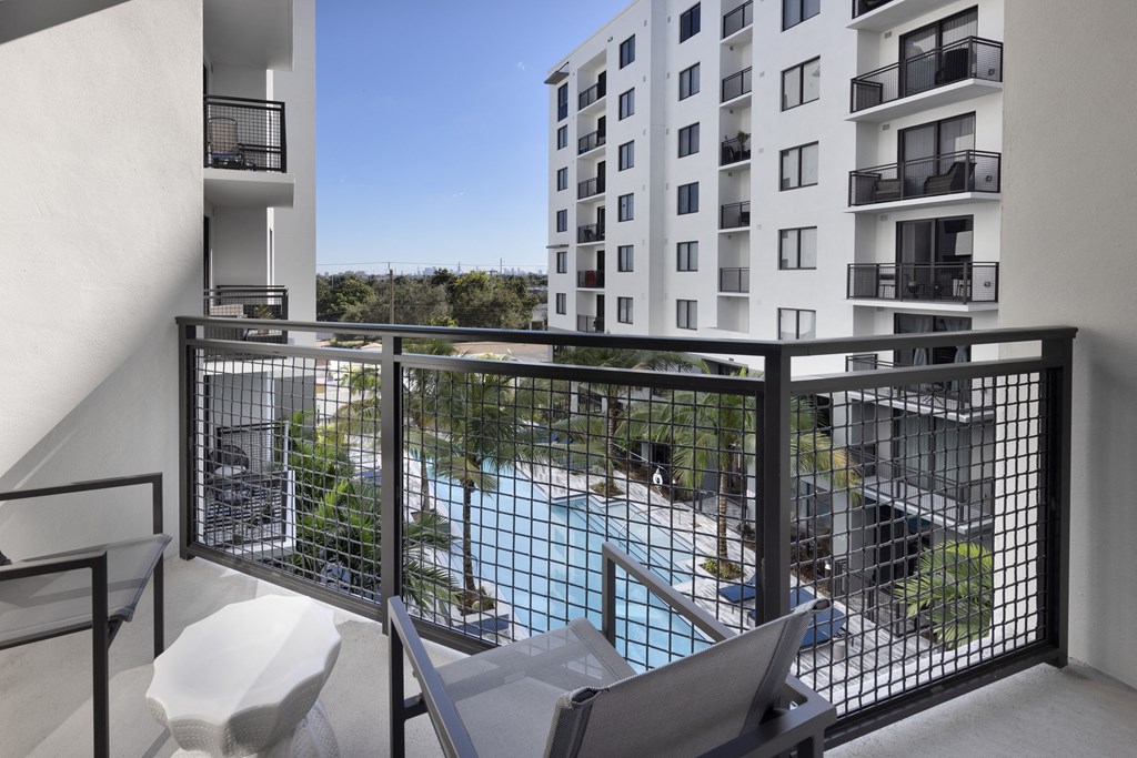 A balcony with a chair and table overlooking a pool.