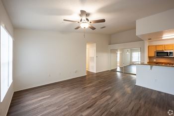 an empty living room with a ceiling fan and a kitchen