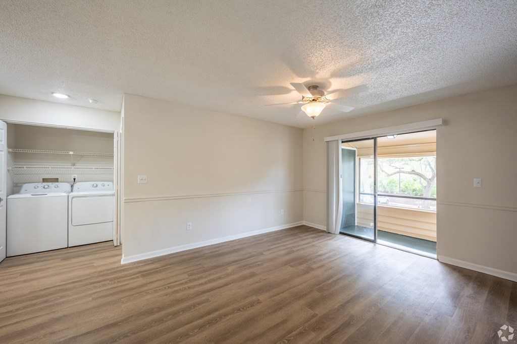an empty living room with a kitchen and a ceiling fan
