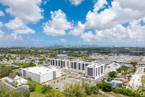 A large white building is surrounded by other buildings and trees.
