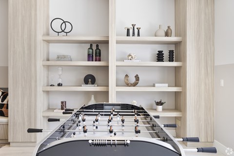 A foosball table is in the middle of a room with shelves on the walls.