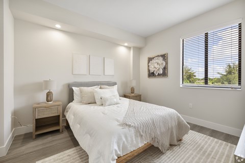 A bedroom with a large bed, a nightstand, and a window with blinds.
