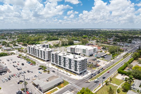 A large white building is surrounded by a parking lot and a road.