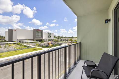 A balcony with a chair and a view of a parking lot and buildings.