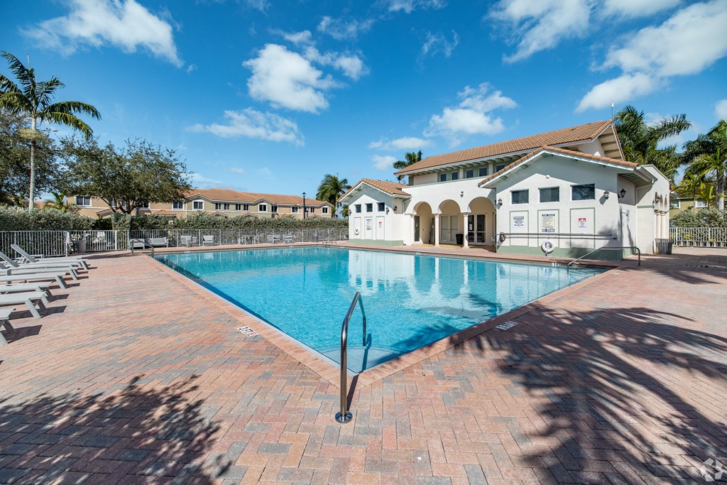 A large swimming pool surrounded by a brick patio and a white building in the background.