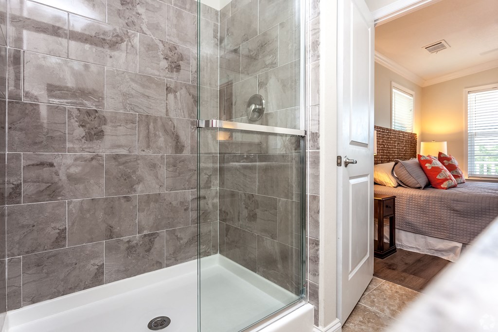 A bathroom with a walk-in shower and a bedroom in the background.