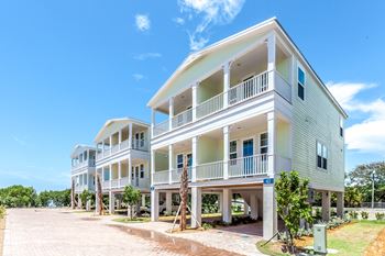A row of white and green townhouses with balconies and trees in front.