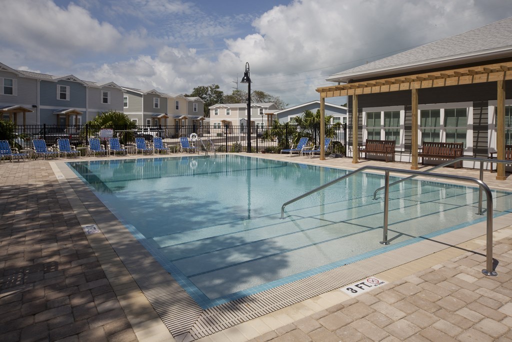 A pool surrounded by a brick patio and a wooden pavilion.