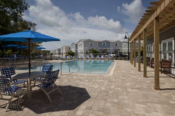 A pool area with a table and chairs and umbrellas.