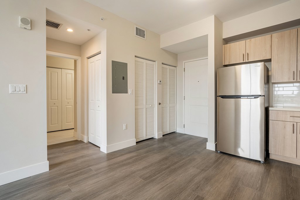 an empty living room with a refrigerator and a kitchen