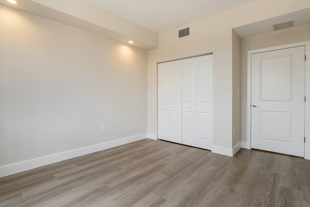 a bedroom with white walls and wood flooring and two closets