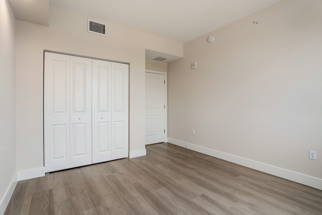 a bedroom with white walls and wood flooring and a closet