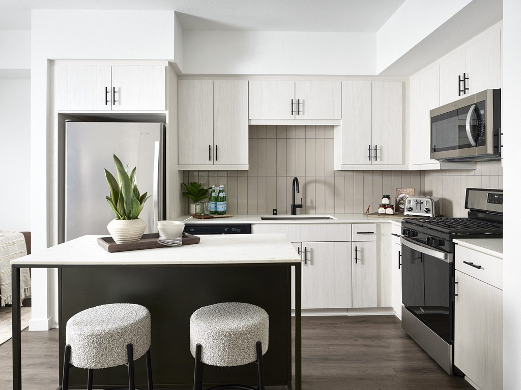a kitchen with white cabinets and a white island with three stools