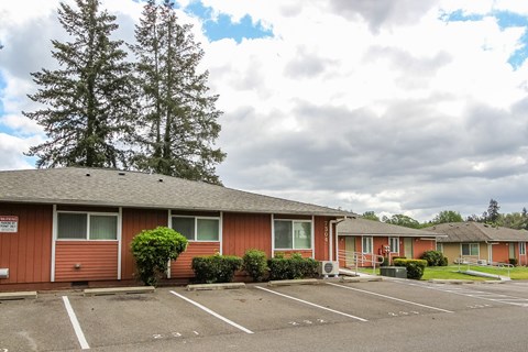 A parking lot in front of a red building with trees in the background.