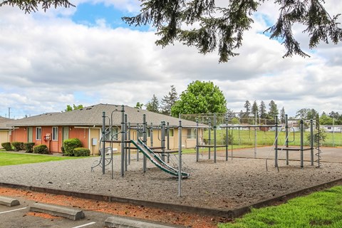A playground with a slide and swings in front of a building.