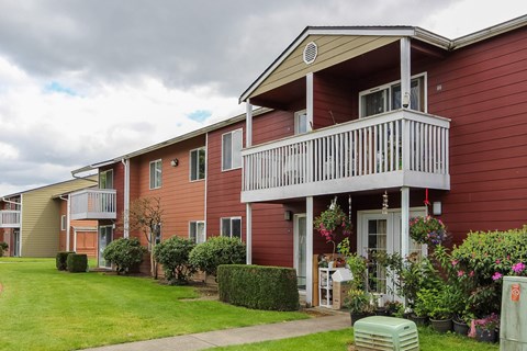 A red building with a balcony and a small garden in front.
