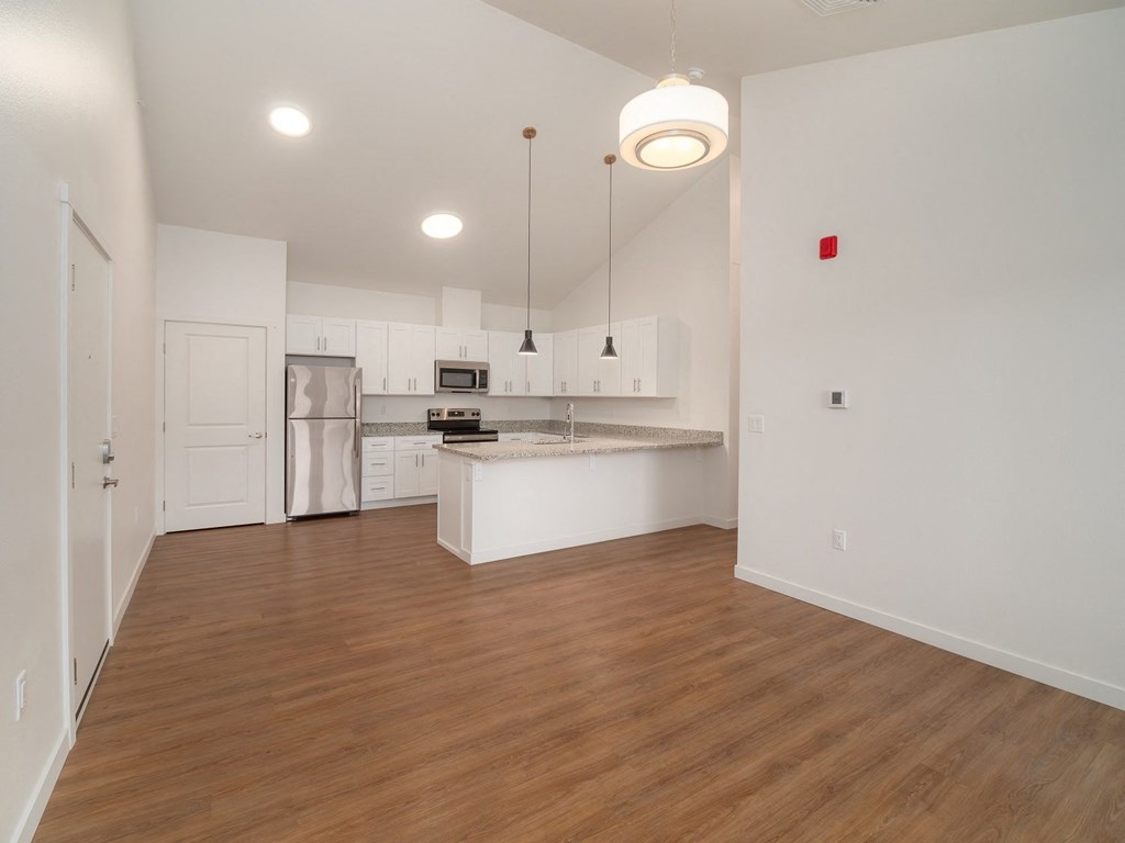 an empty living room with a kitchen with white cabinets