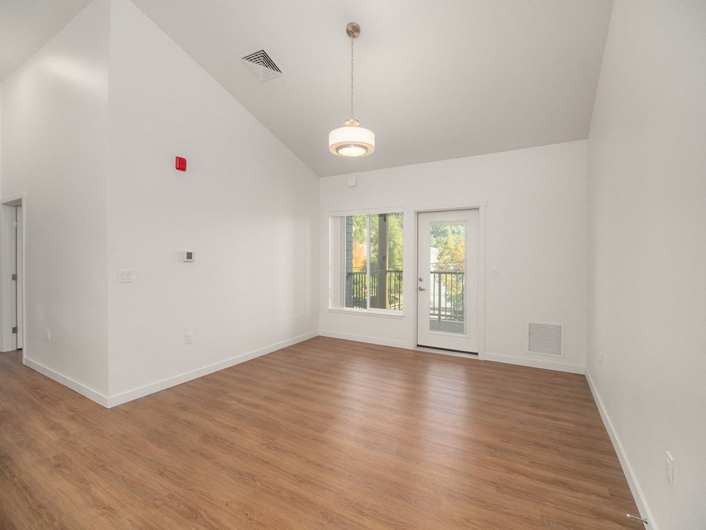 a living room with white walls and wood floors and a door to a balcony