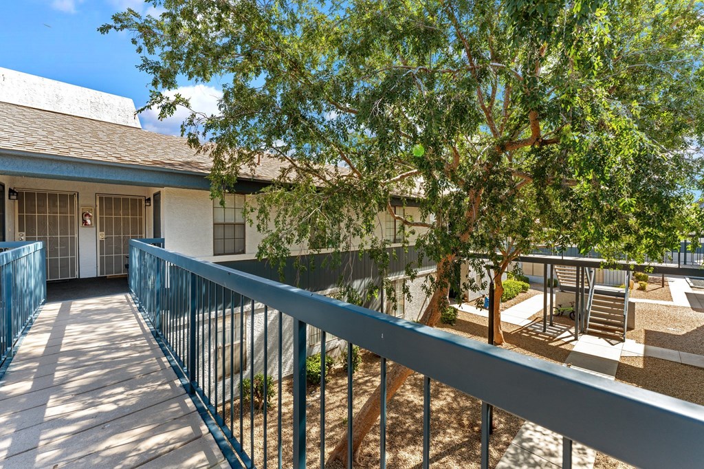 A balcony with a railing overlooks a courtyard with a tree and a building.