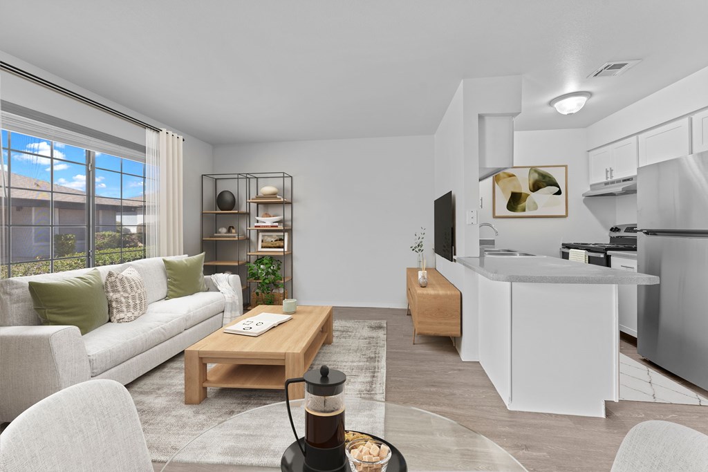 A modern living room with a white sofa, a wooden coffee table, and a kitchen area in the background.