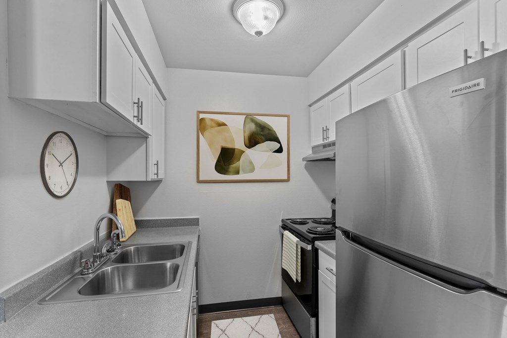 A modern kitchen with a stainless steel refrigerator, a sink, and a clock on the wall.
