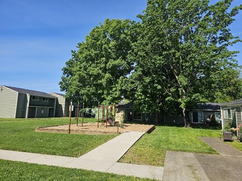 A playground with a slide and swings is surrounded by a grassy area and trees.