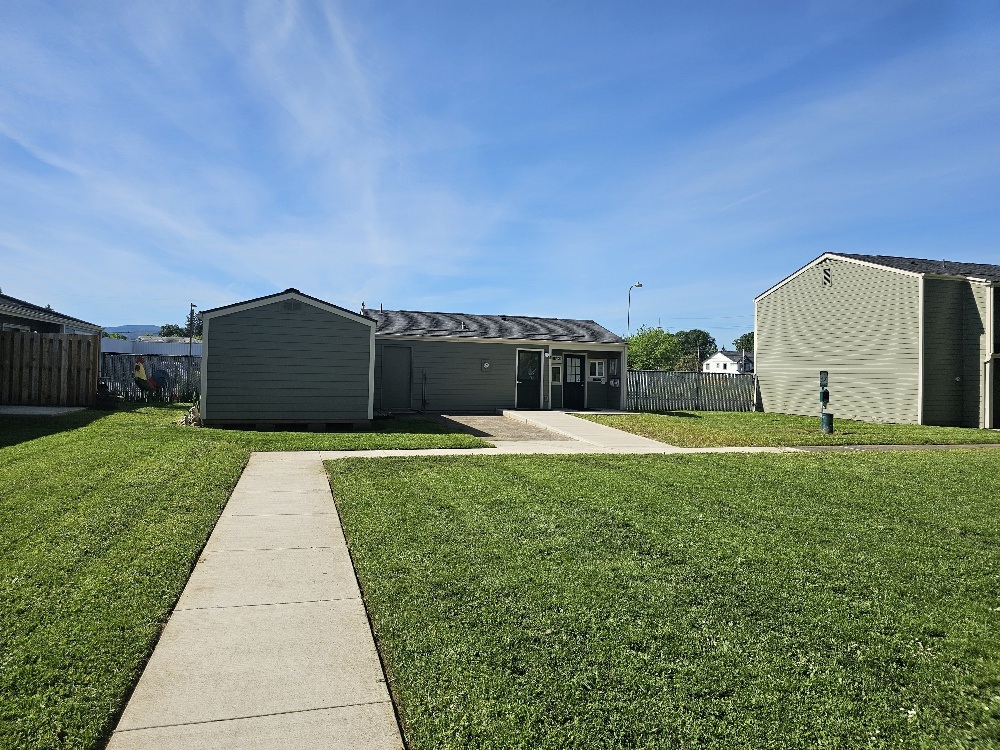 A grassy area with a concrete walkway leading to a building with a grey roof.