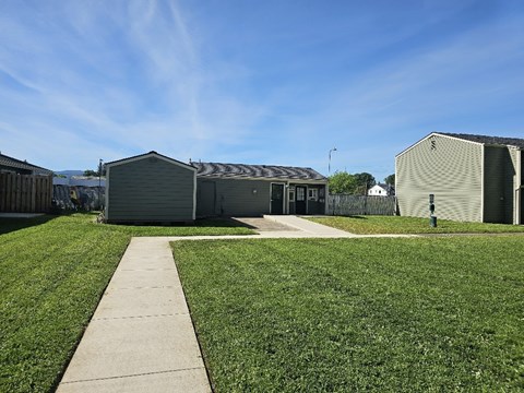 A grassy area with a concrete walkway leading to a building with a grey roof.