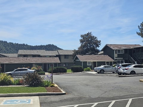 A parking lot with a building in the background and a car parked in the handicap spot.