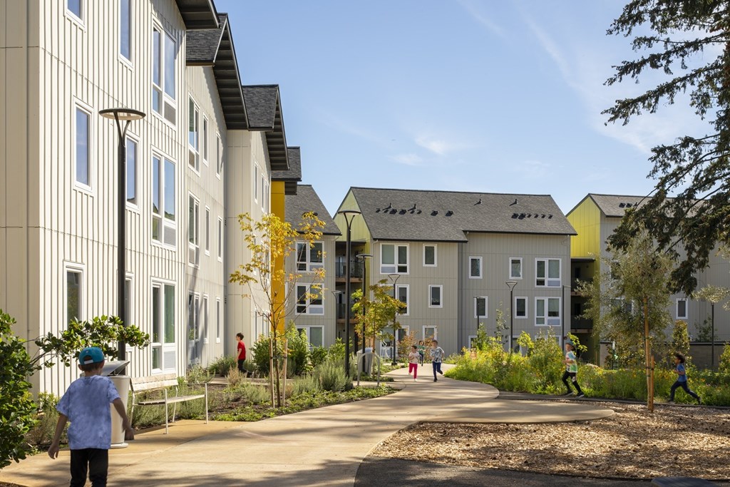 A person in a blue shirt is walking down a path in front of a building.