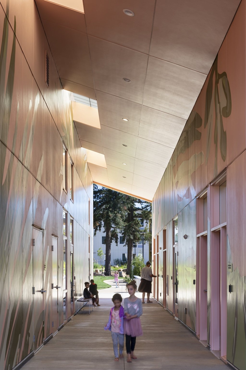A long hallway with pink walls and a girl walking down it.