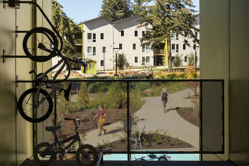 A bicycle is hanging on a rack in a room with a view of a courtyard.