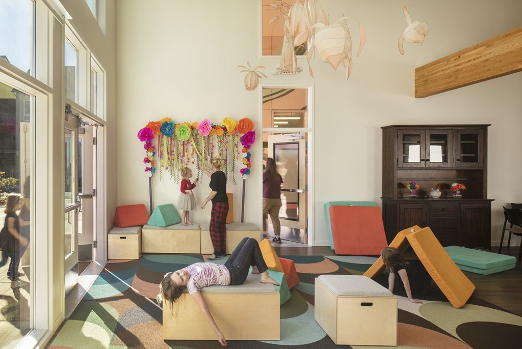 A woman is lying on a colorful mat in a room with children's play areas.