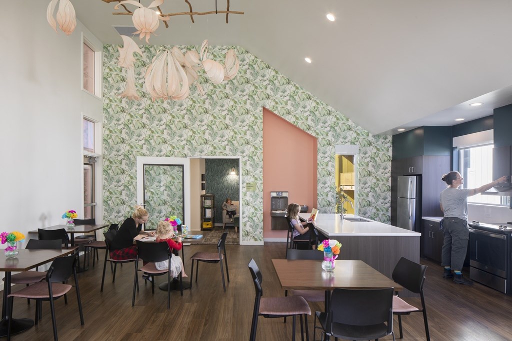 A woman and a child are sitting at a table in a room with a green floral wallpaper.