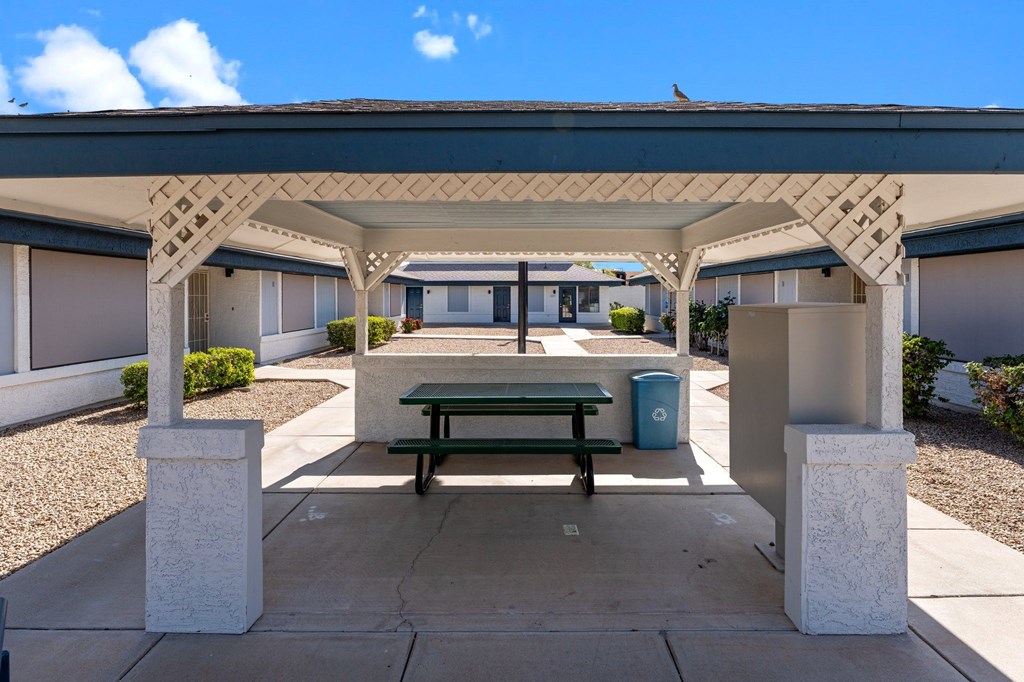 A covered patio area with a bench and a trash can.