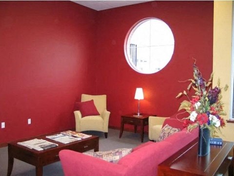 A living room with a pink couch, a yellow chair, a coffee table, and a round window.