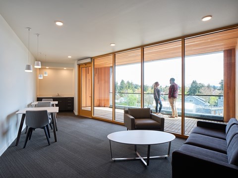 A modern living room with a grey carpet and a large window overlooking a green landscape.