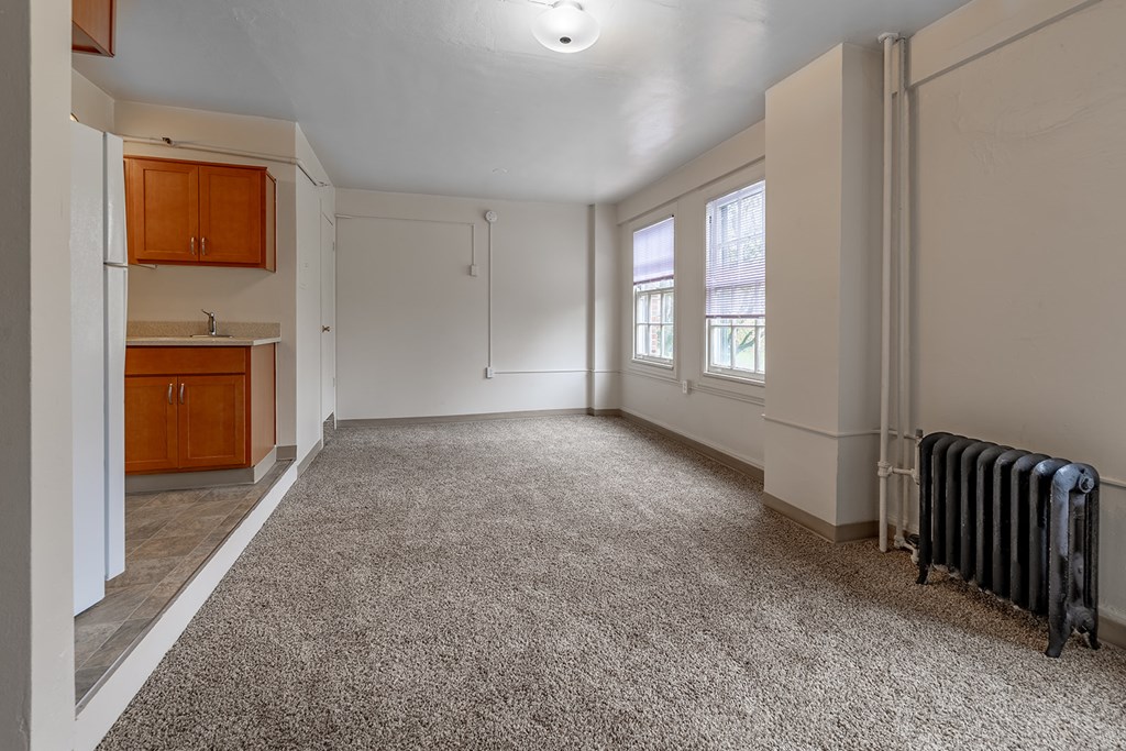 A spacious room with a carpeted floor and a radiator on the wall.