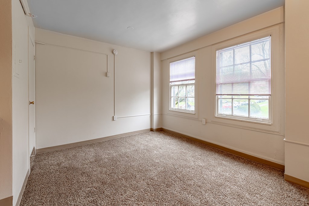 A room with a carpeted floor and two windows.