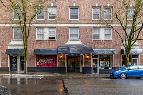 A blue car is parked in front of a building with a red awning.