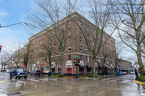 A large brick building sits at a street corner with cars parked on the street.